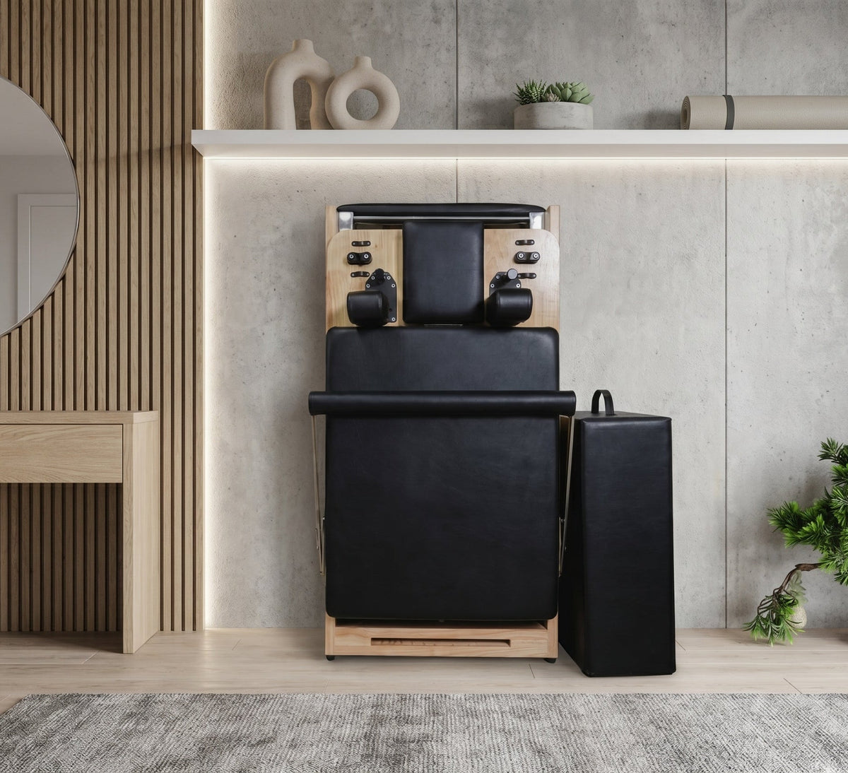 Front view of folded black leather reformer against concrete wall showing shoulder rests and accessory block.