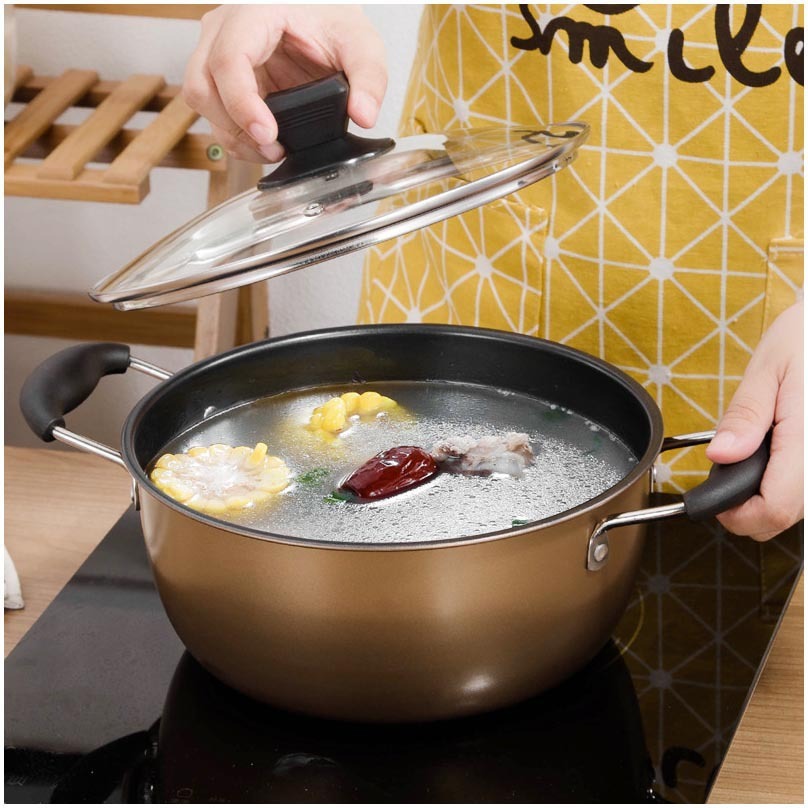 Person lifting glass lid off gold stockpot boiling soup with corn and dates on induction cooktop