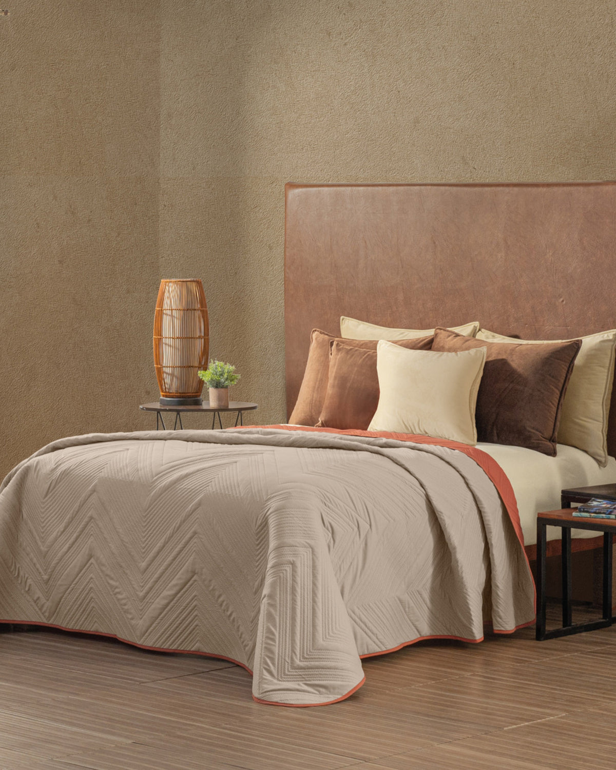 Beige chevron quilted bedspread with terracotta piping on a brown leather headboard beside rust and cream velvet pillows