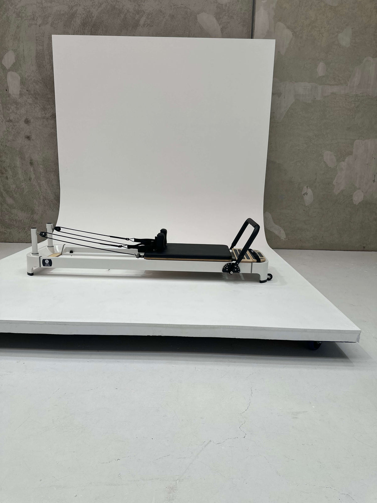 Side view of black upholstery reformer on white platform highlighting sleek frame