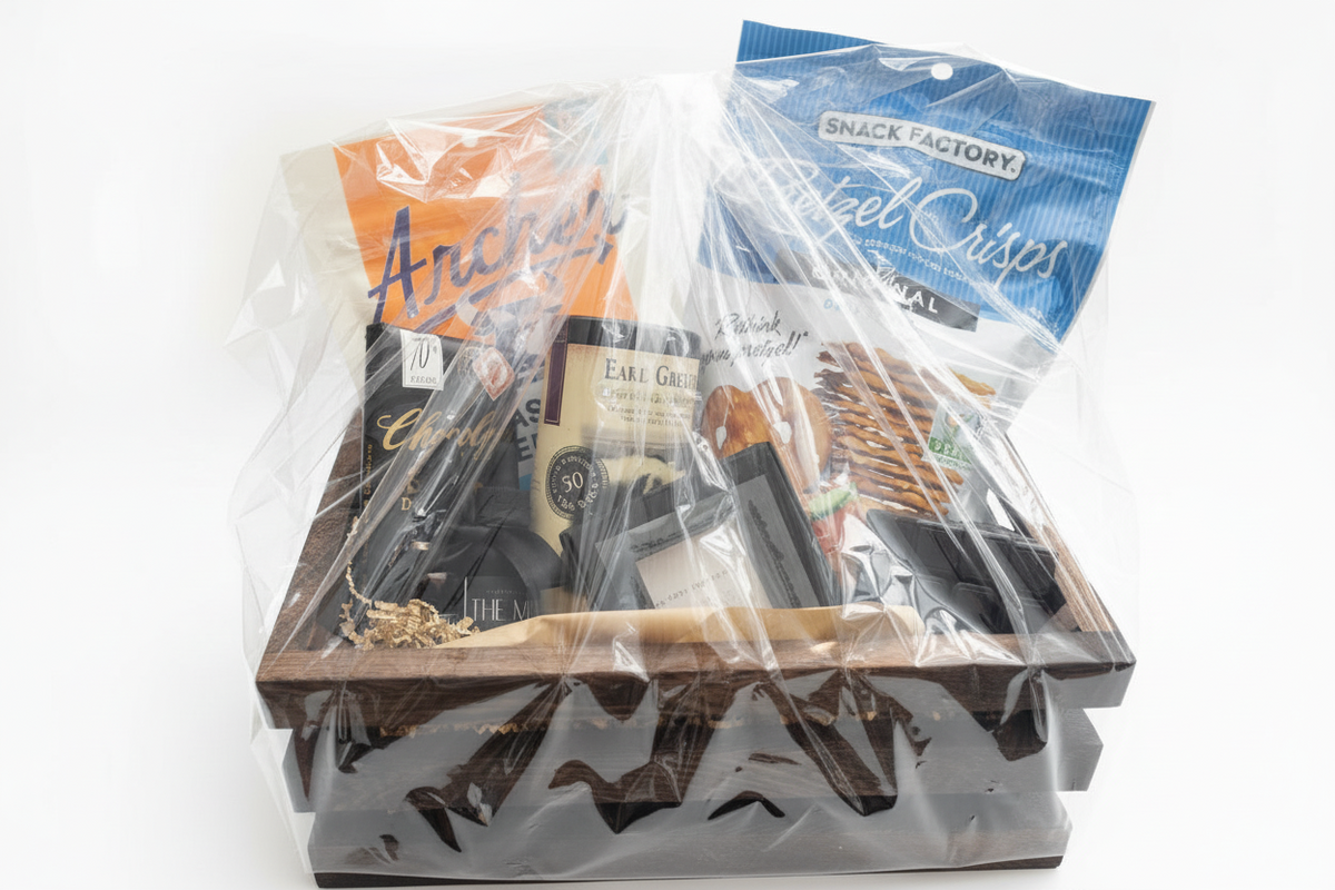 High-angle glossy cellophane-wrapped basket showing orange jerky bag, blue pretzel bag, tea tin, and grooming products