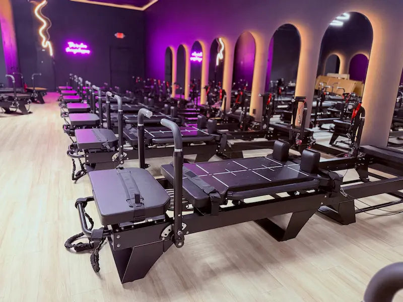 Rows of black Sculptformer machines with padded seats aligned on light wood flooring under purple ambient lighting