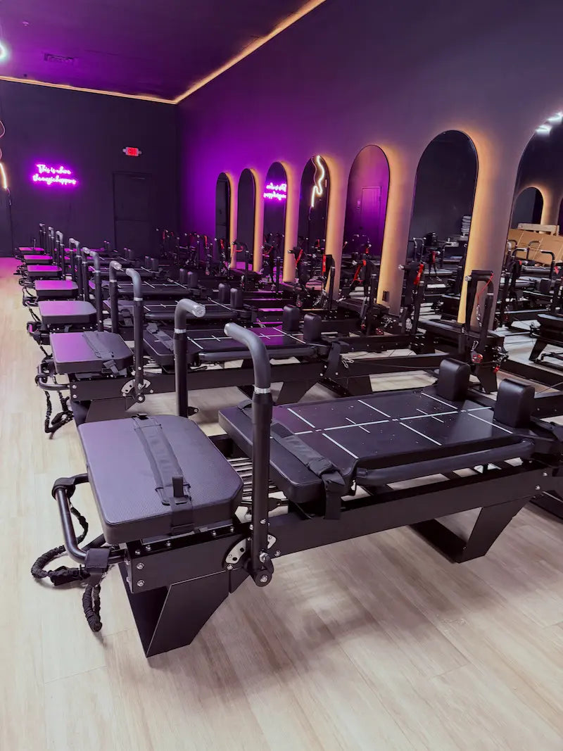 High-angle view of black Lagree-style machines in neat rows with padded carriages, shoulder rests, and resistance bands