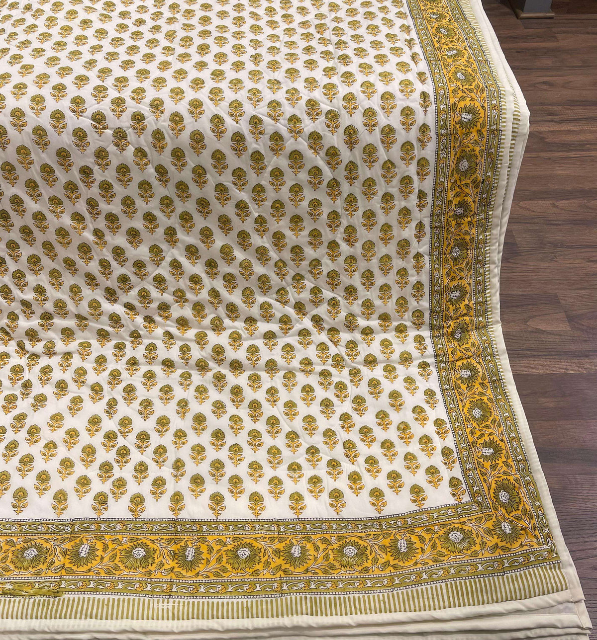 High-angle close-up of cream comforter on dark wood floor highlighting olive green and mustard yellow block print