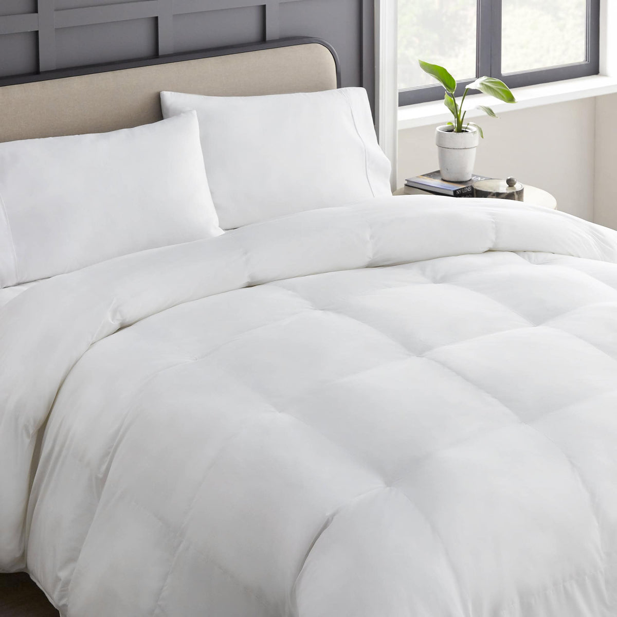 White hypoallergenic comforter styled on bed with grey paneled headboard and natural window light