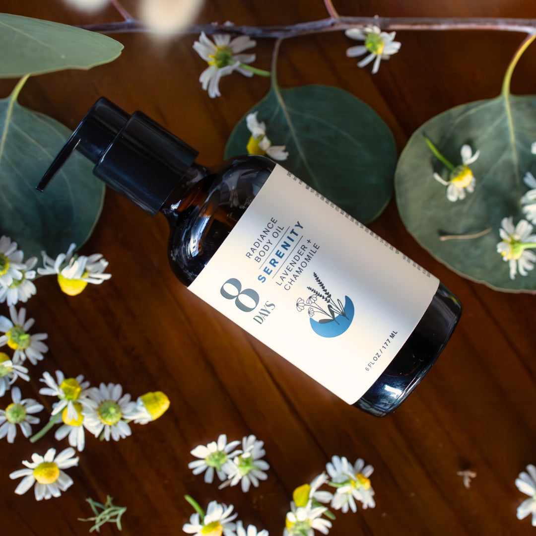 Amber glass pump bottle of lavender body oil on wood with chamomile flowers and eucalyptus leaves