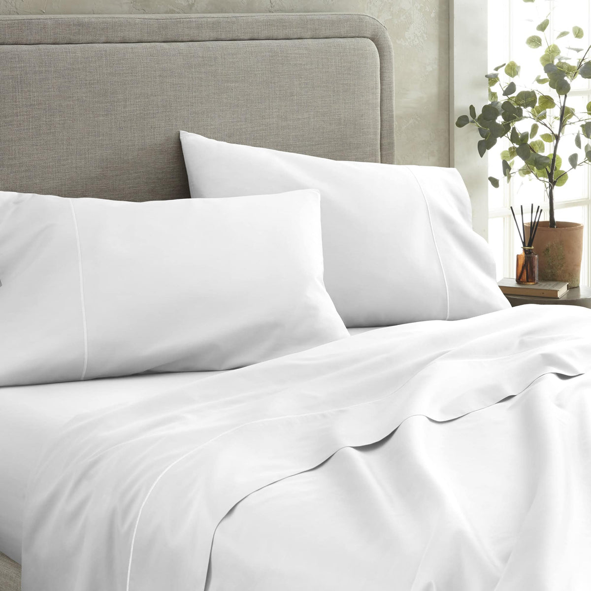 Crisp white 500 TC sateen pillowcases with piping on bed against grey headboard