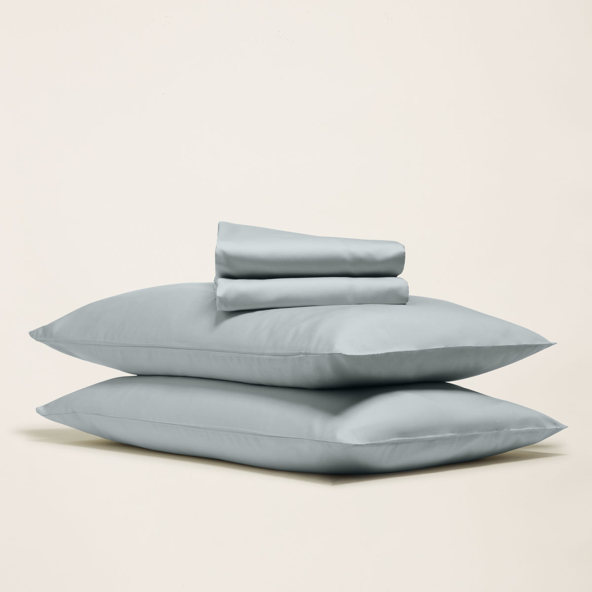 Stacked slate-blue pillowcases with a neatly folded flat sheet resting on top against a neutral background