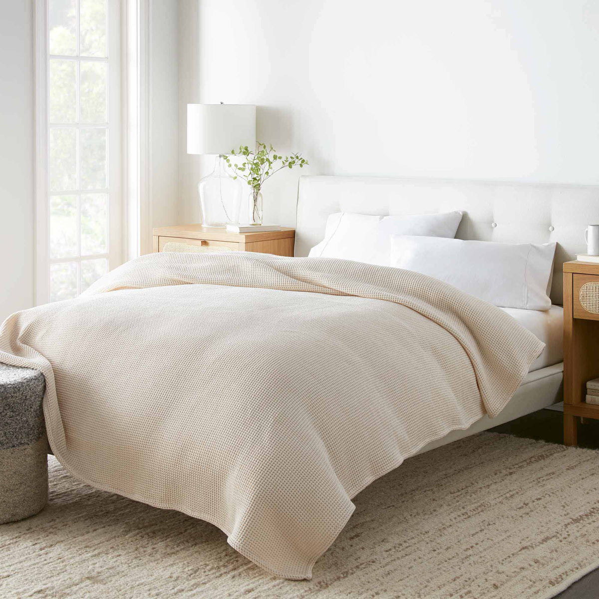 Cream organic cotton waffle blanket draped over bed in minimalist bedroom