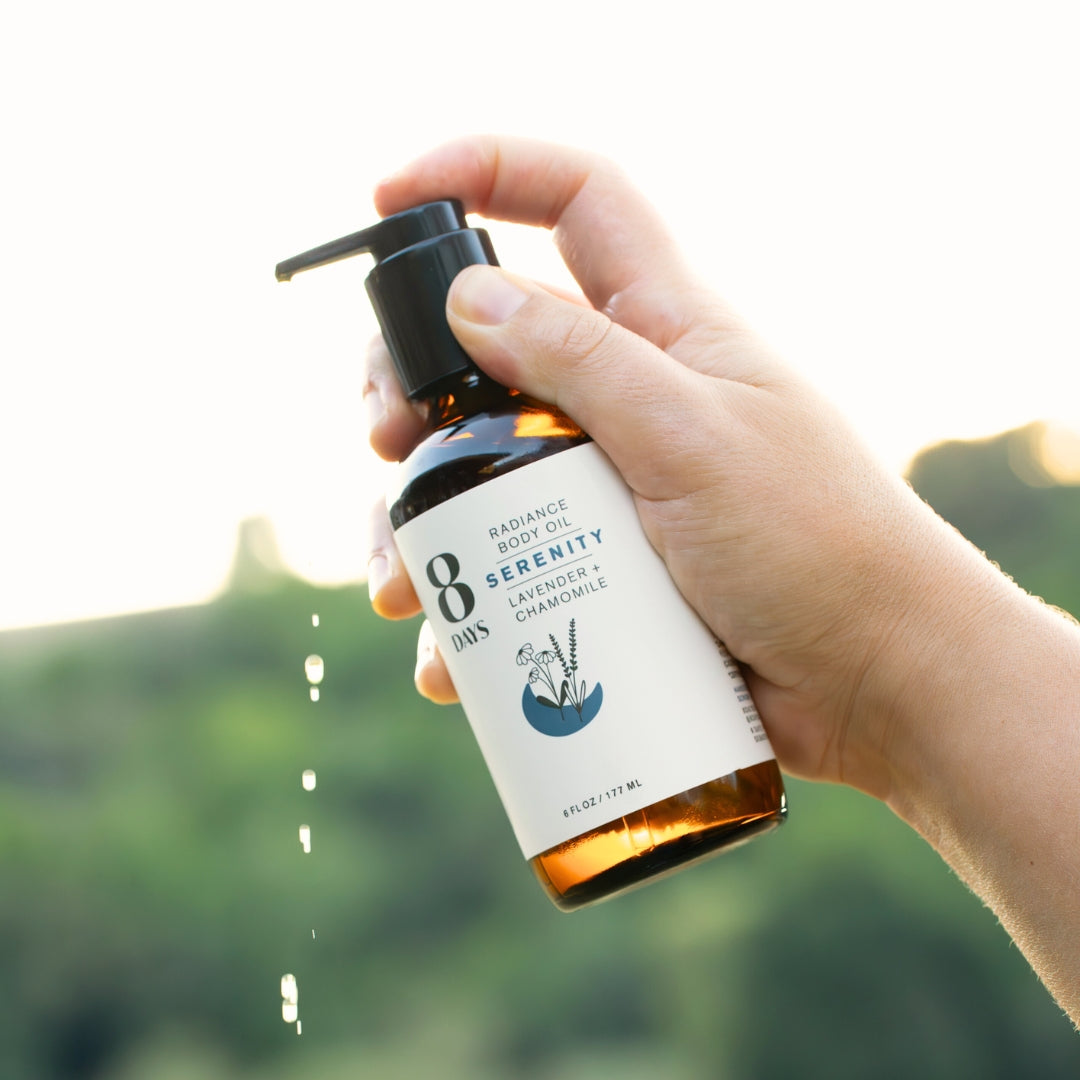 Hand holding amber bottle showing oil droplets falling from black pump dispenser outdoors