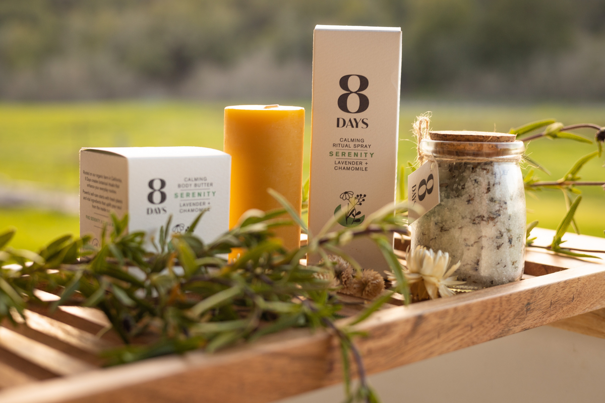 Product line on wood surface surrounded by fresh rosemary sprigs, focusing on 'Serenity Lavender + Chamomile' text on boxes