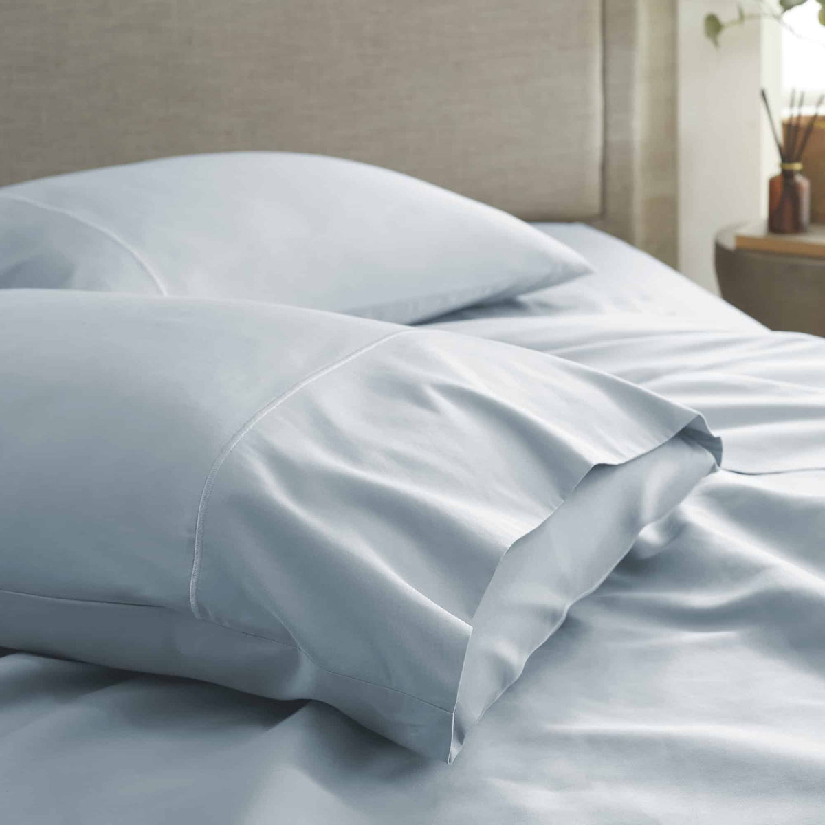 Light blue sateen pillowcases showing sheen and folds on bed