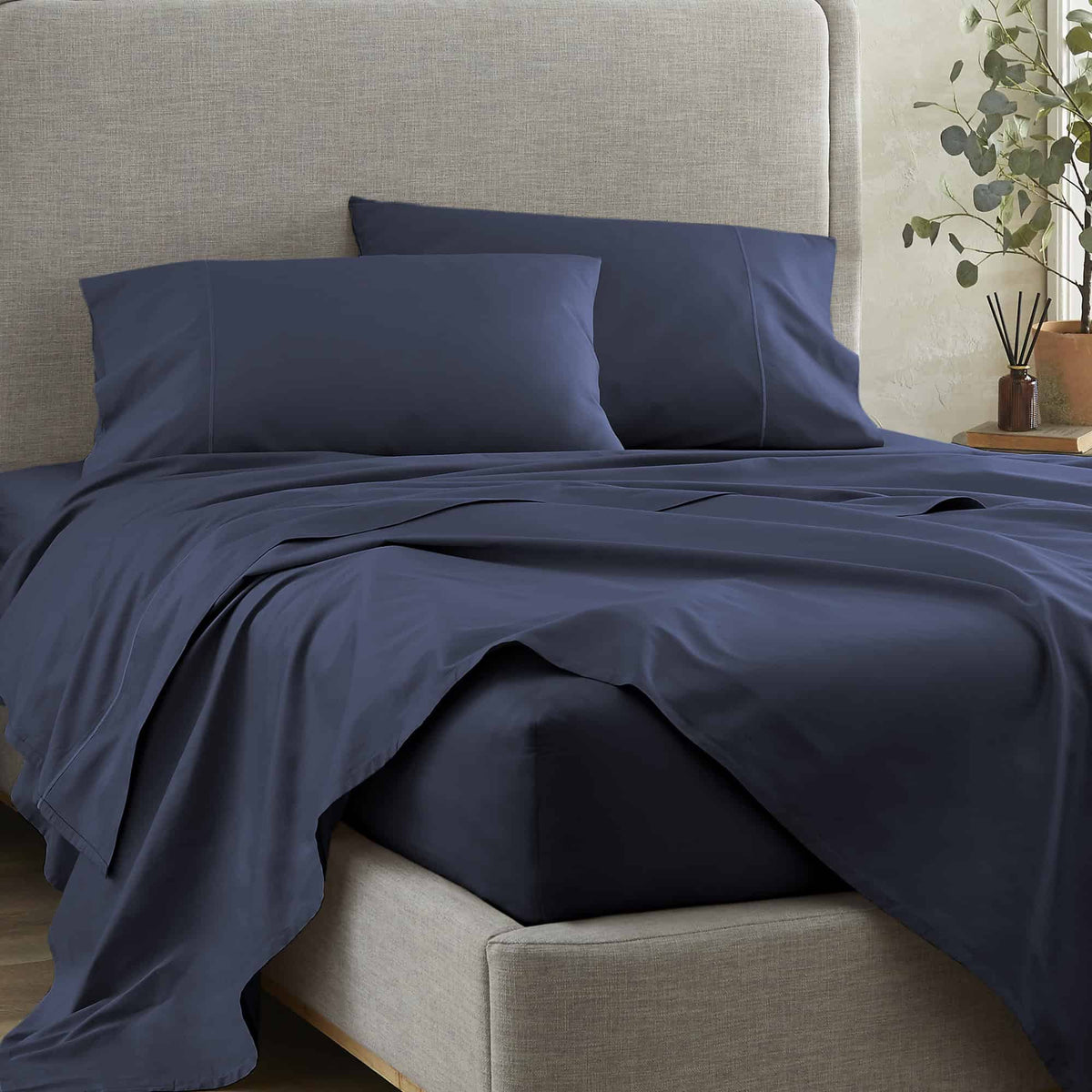 Navy blue sheet set and pillowcases on grey upholstered bed frame