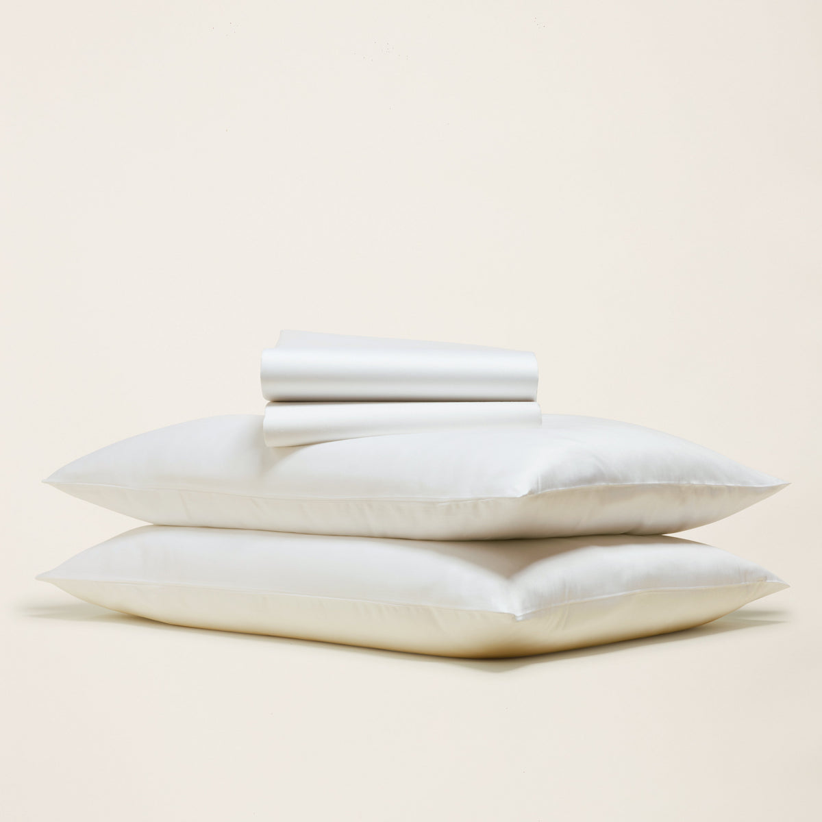 Two stacked white pillowcases with a rolled flat sheet highlighting crisp hotel-grade sateen texture