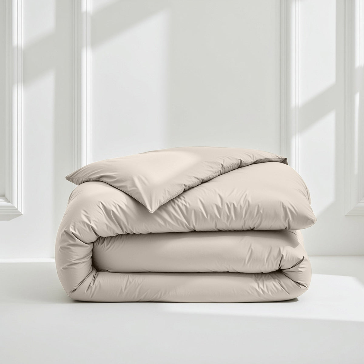 Folded taupe sateen duvet cover on white surface with window shadows