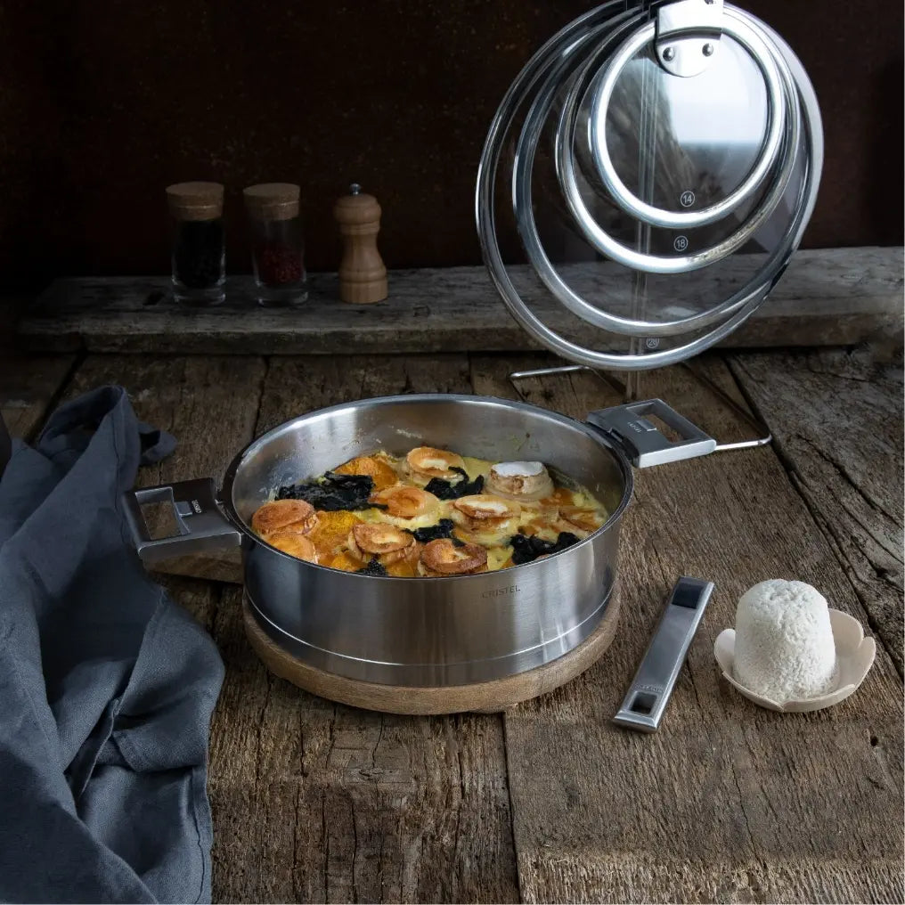 Stainless steel pot with scallops and seaweed on wooden board beside removed handle