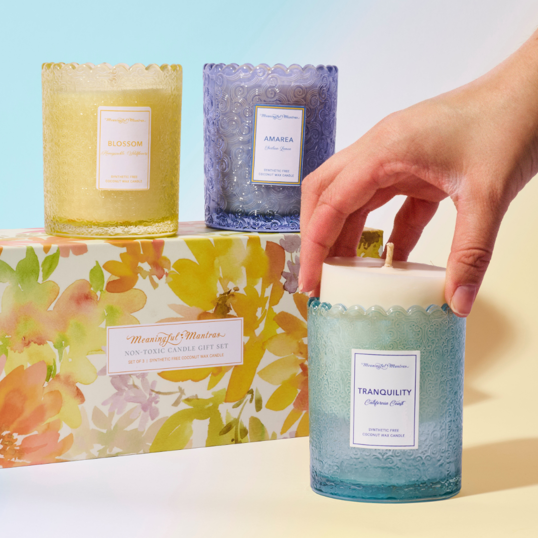 Three colored candles in yellow purple and blue arranged around floral gift box with hand lifting wax refill