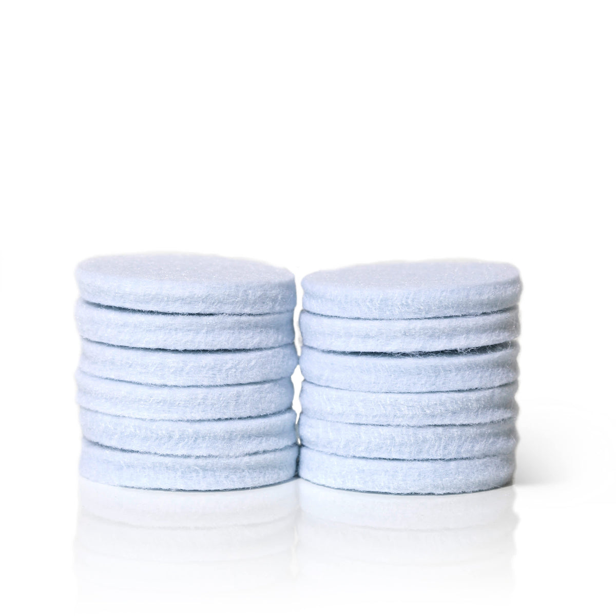 Two neat stacks of light blue fibrous circular replacement pads arranged side-by-side on reflective white surface