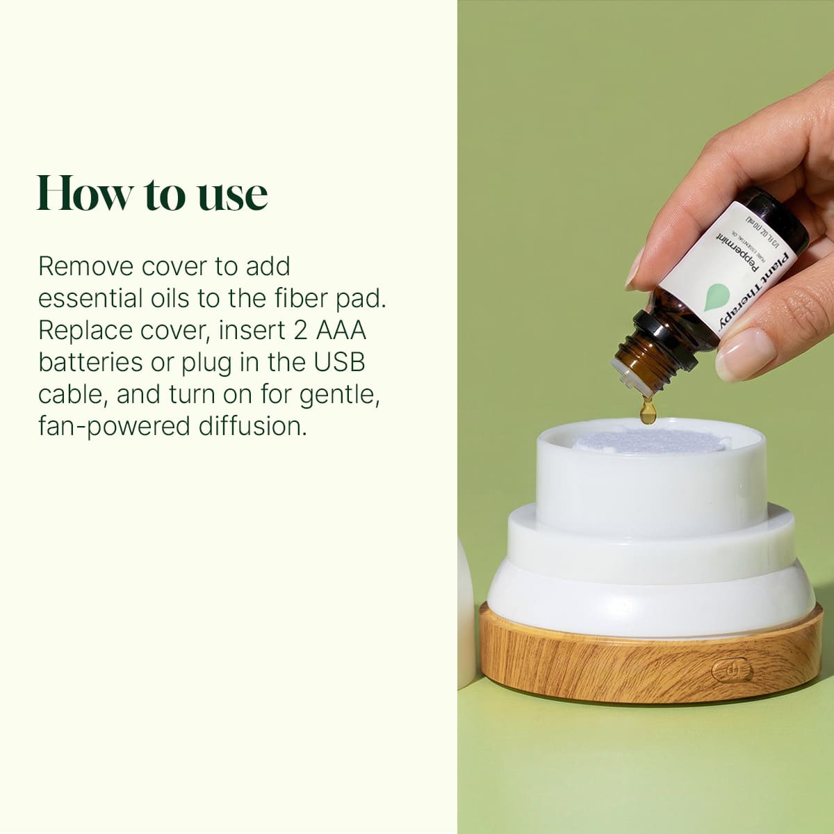 Hand pouring essential oil onto white fiber pad of disassembled AuraDrop diffuser sitting on oak wood base