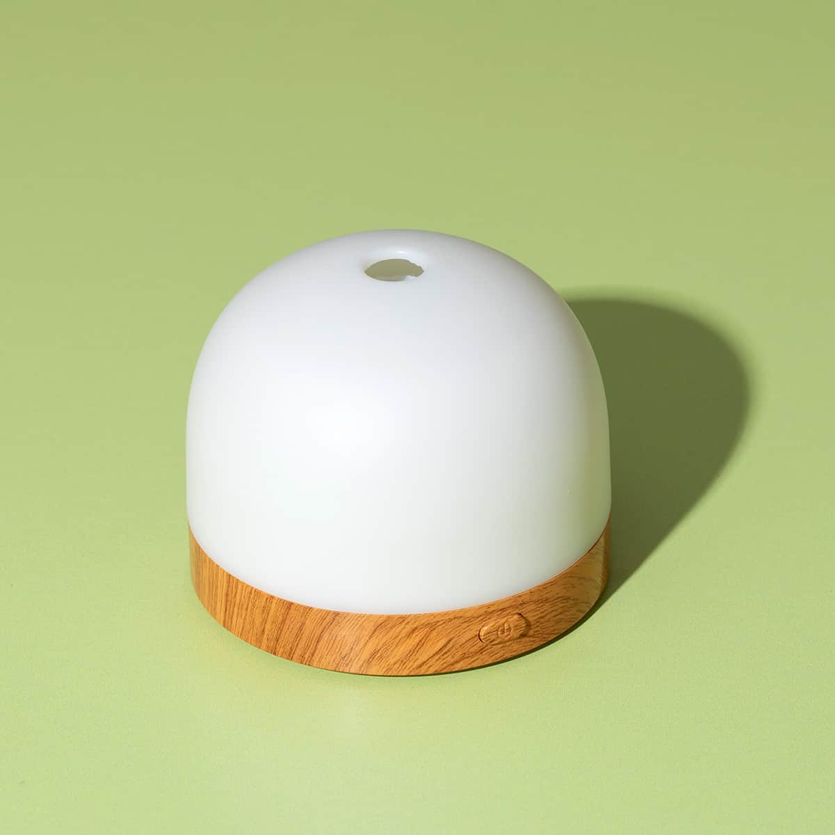 High-angle close-up of assembled AuraDrop diffuser with smooth white dome top and engraved power button on green surface