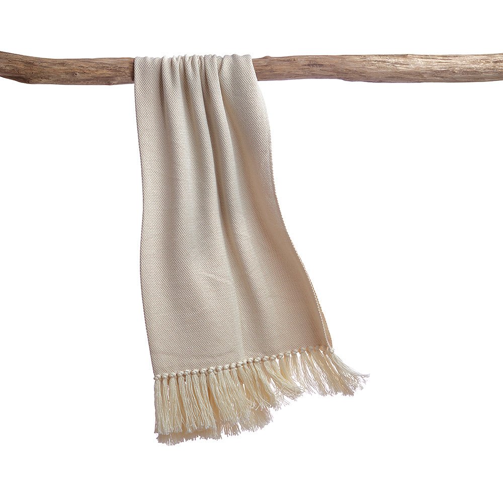 Ivory melange twill throw blanket draped over a rustic wooden branch, showcasing long knotted fringe trim against a white