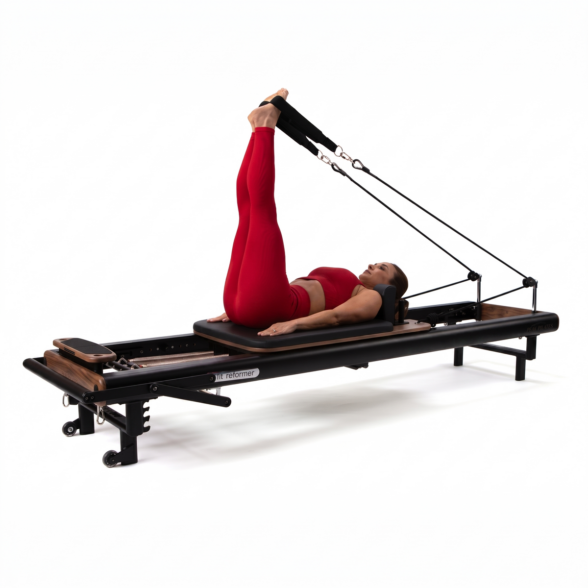Woman in red activewear performing leg exercise on black Peak Pilates fit Reformer with Walnut accents, legs extended into