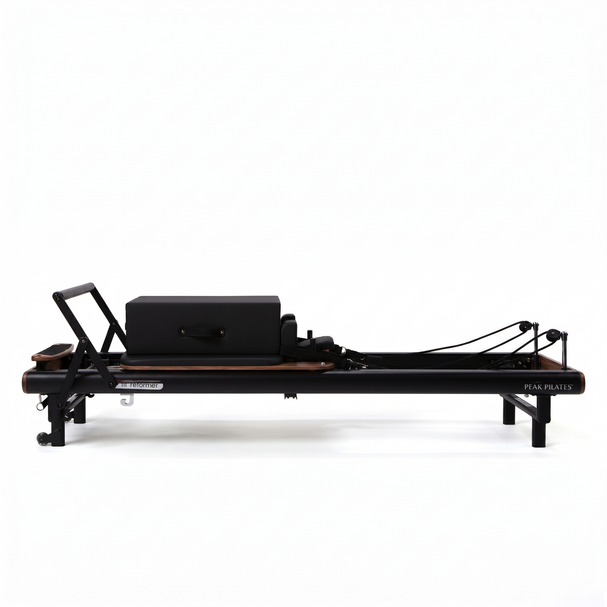 Side profile of black Peak Pilates fit Reformer with walnut wood footbar, long black box on carriage, and brand logo visible
