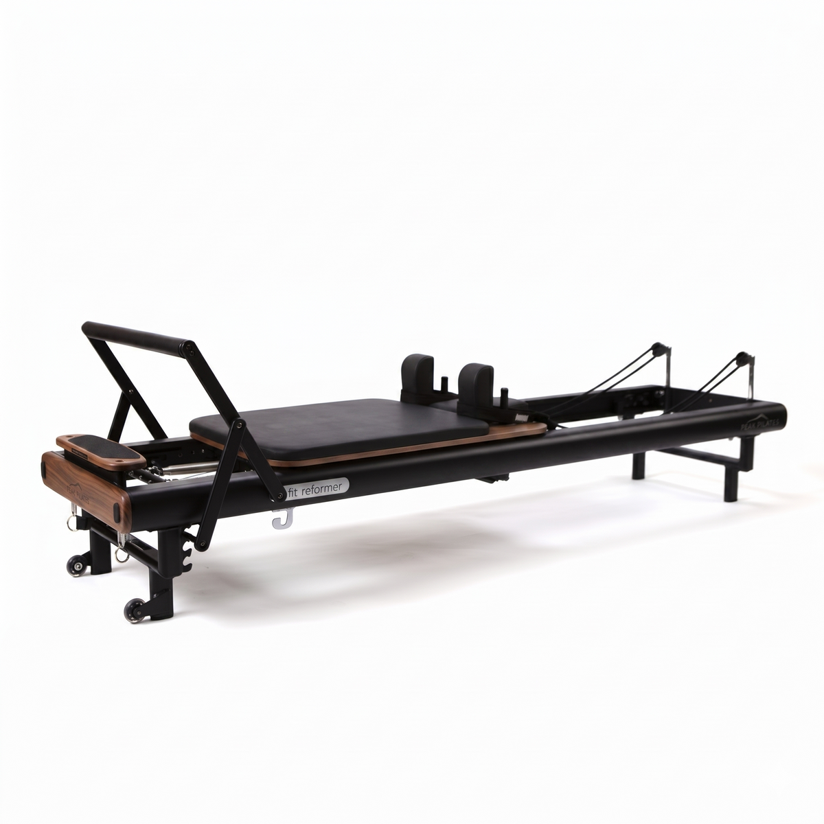 Three-quarter angle of black fit Reformer with walnut details, displaying gliding carriage, shoulder rests, cable system, and