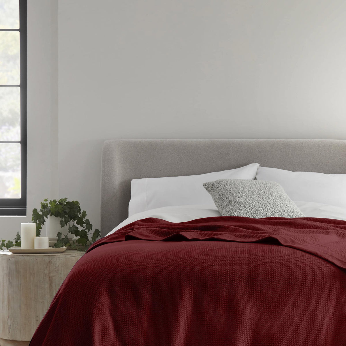 Deep burgundy red woven blanket spread on bed with grey headboard and white pillows