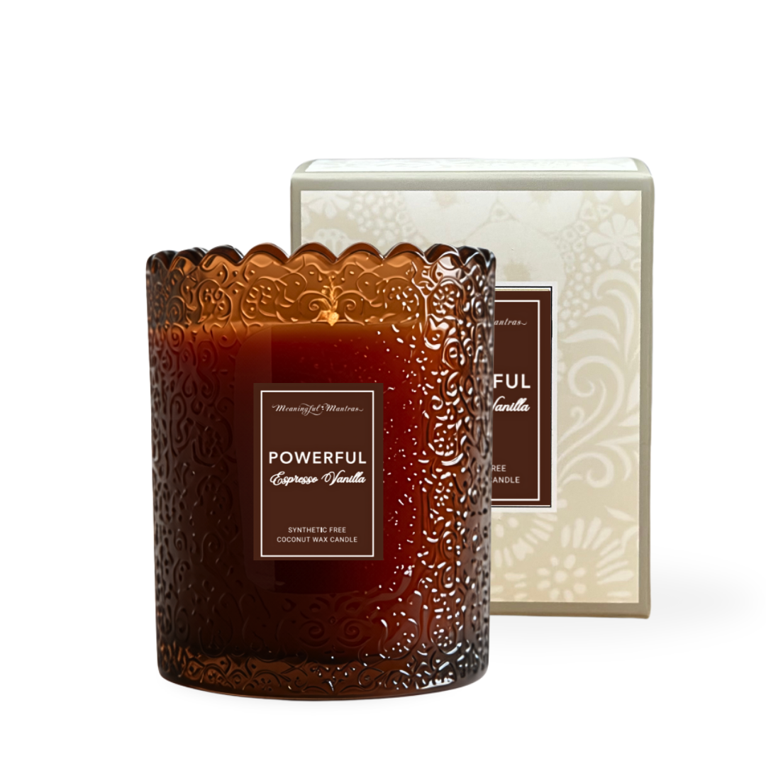 Amber glass candle jar with embossed floral scrollwork and scalloped rim beside cream damask box