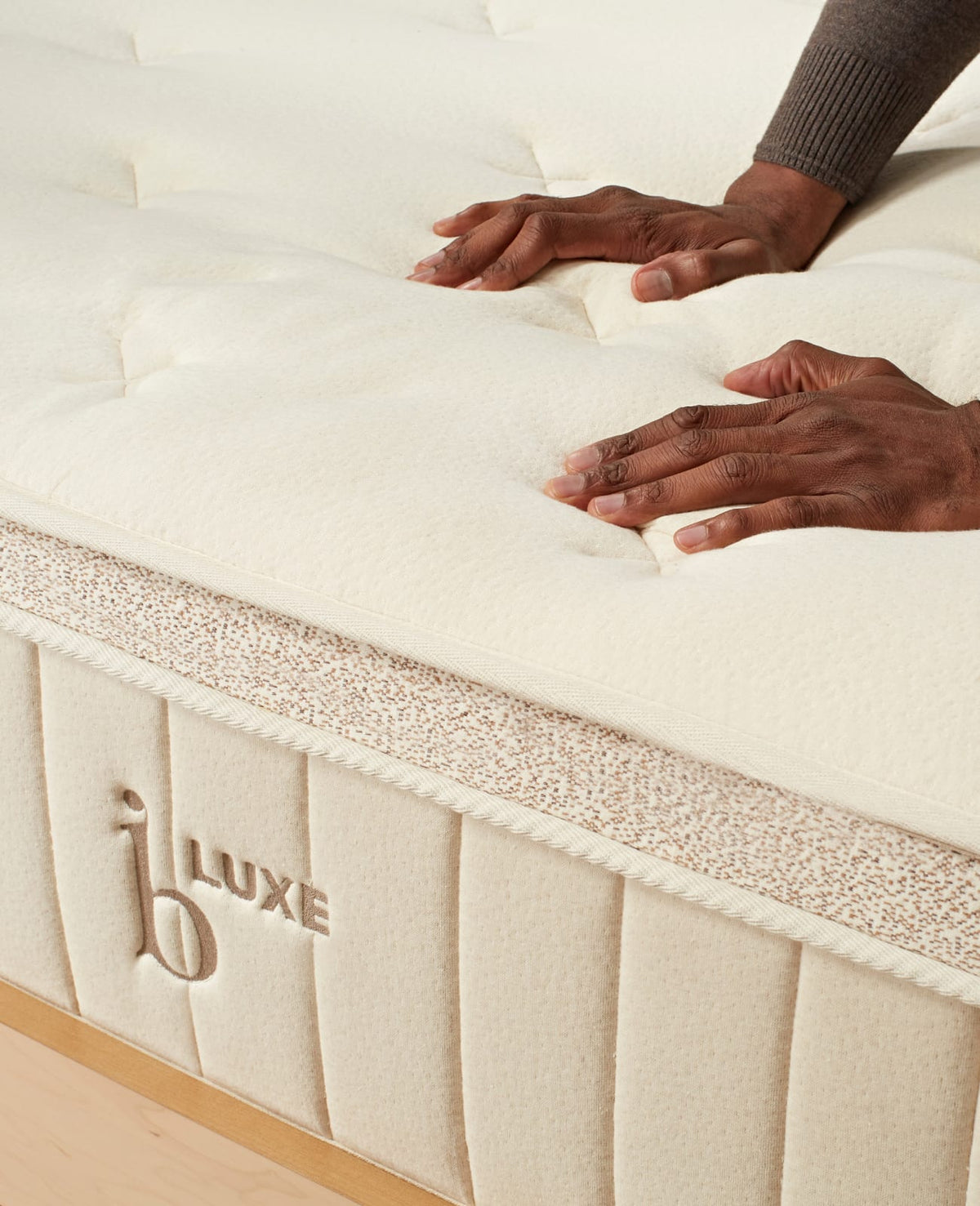 Hands pressing into cream quilted cashmere top of organic hybrid mattress with rope edge and embroidered logo