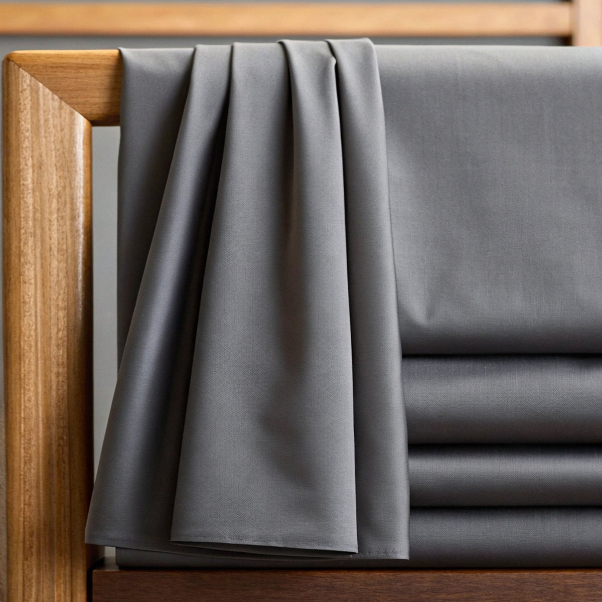 Folded charcoal grey sheet draped over light wood bed frame corner highlighting fine matte weave and smooth surface