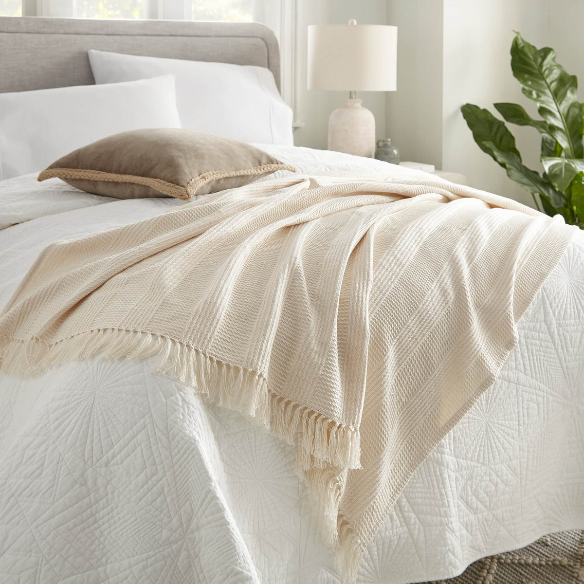 Cream textured throw styled at foot of bed with white quilted bedding and taupe pillow