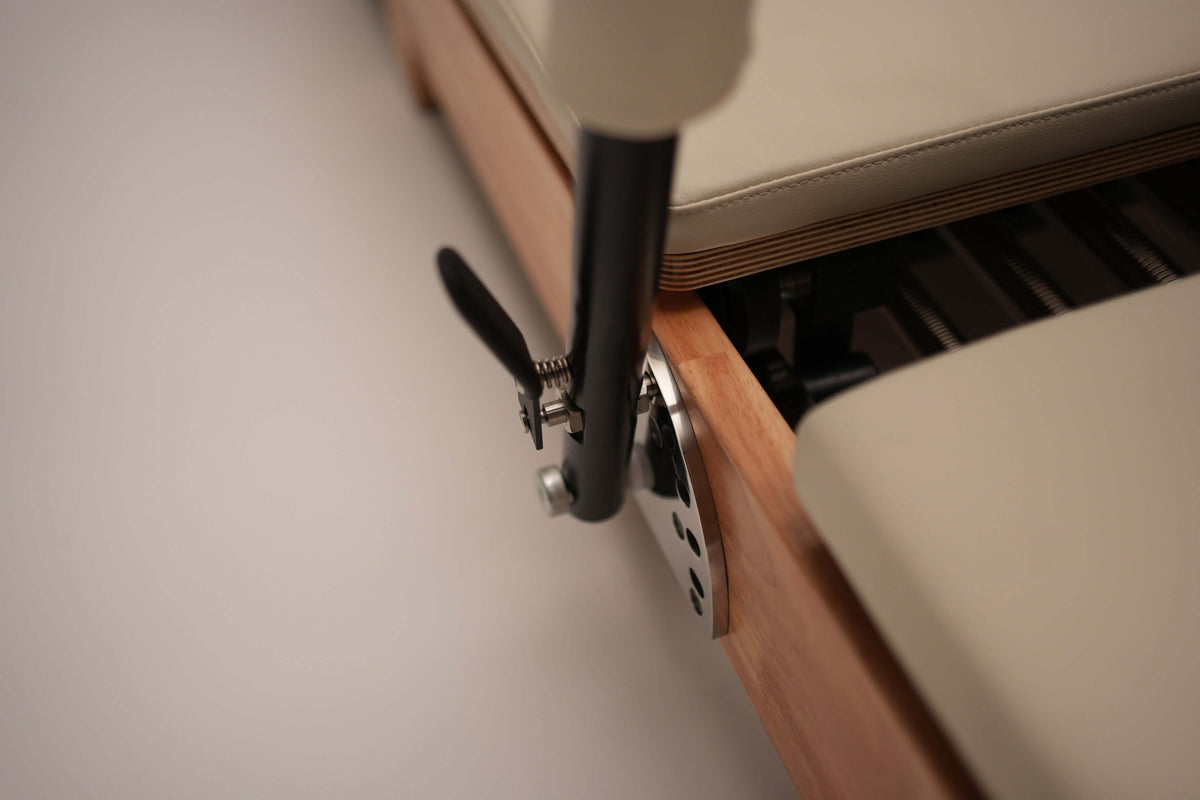 Close-up of footbar adjustment mechanism showing black lever, silver locking knob, and perforated metal plate on wooden frame