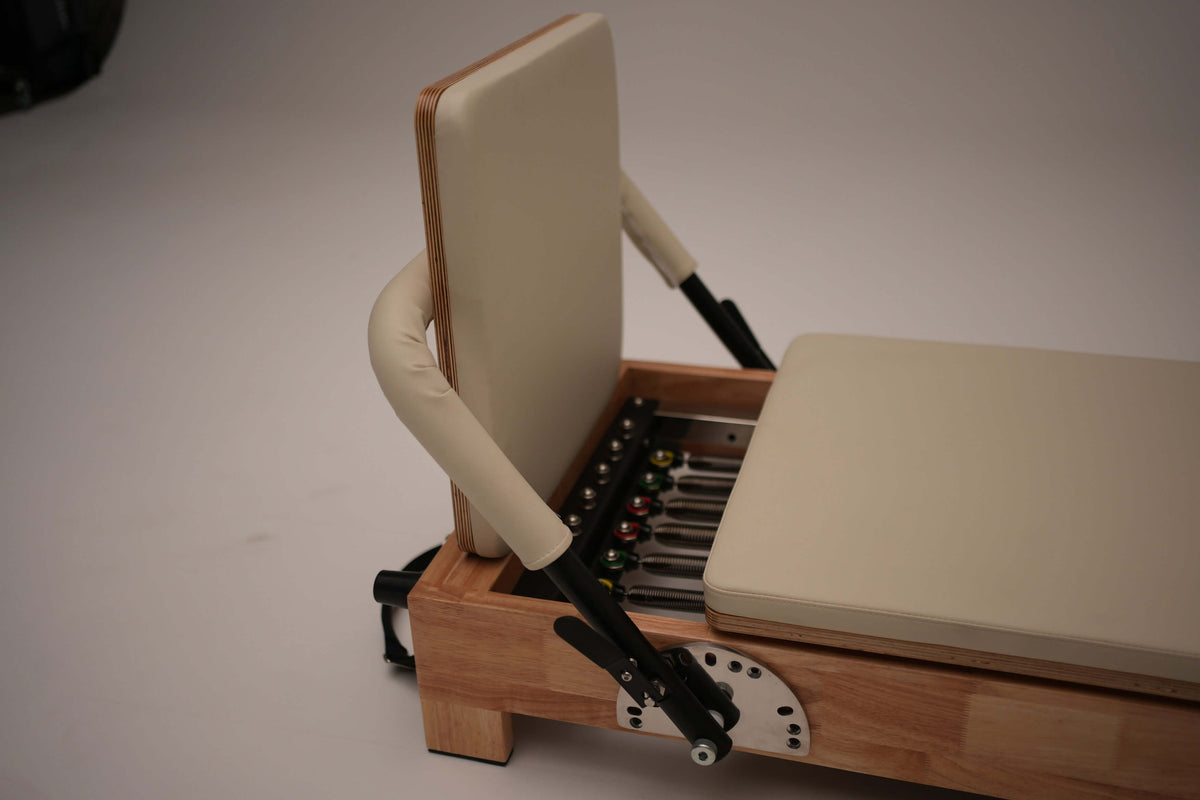 Angle of reformer head end showing layered plywood backrest, curved armrests, and exposed 6-spring resistance system with
