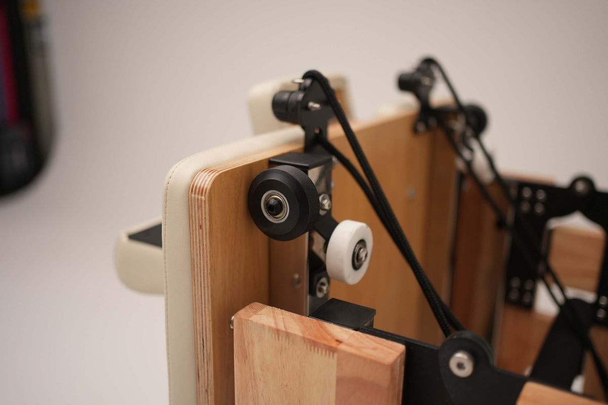 Macro close-up of headstock assembly with black pulley wheels, tension ropes, and layered light wood frame edge details
