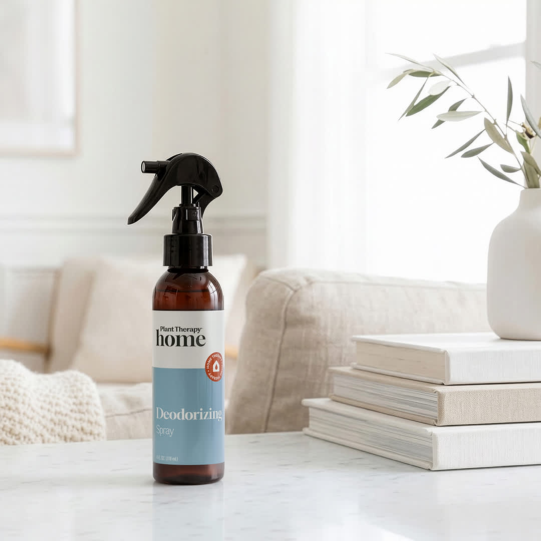 Amber spray bottle standing on white marble table beside books and olive branches