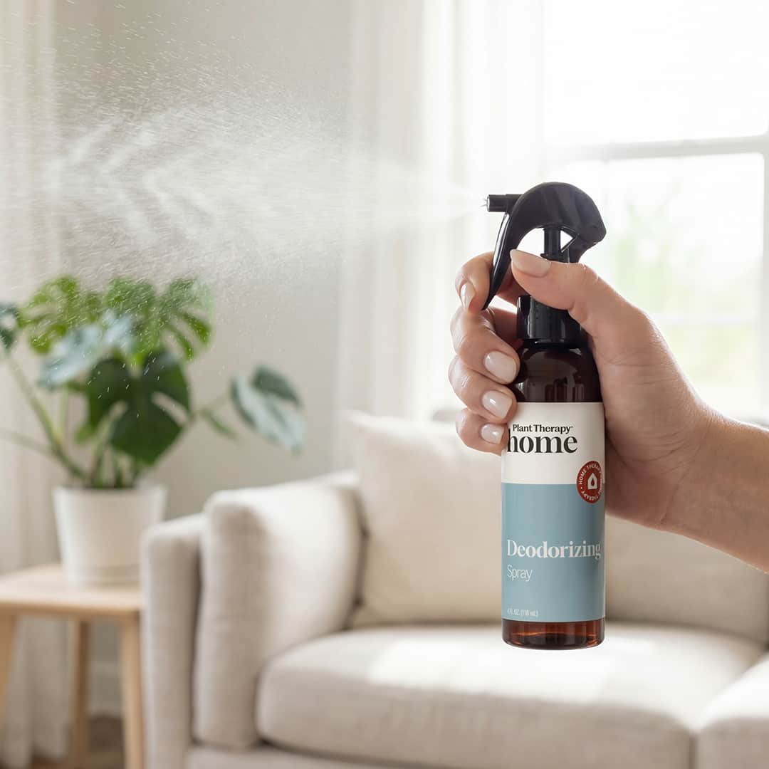 Hand misting amber spray bottle in bright living room near sofa and plant