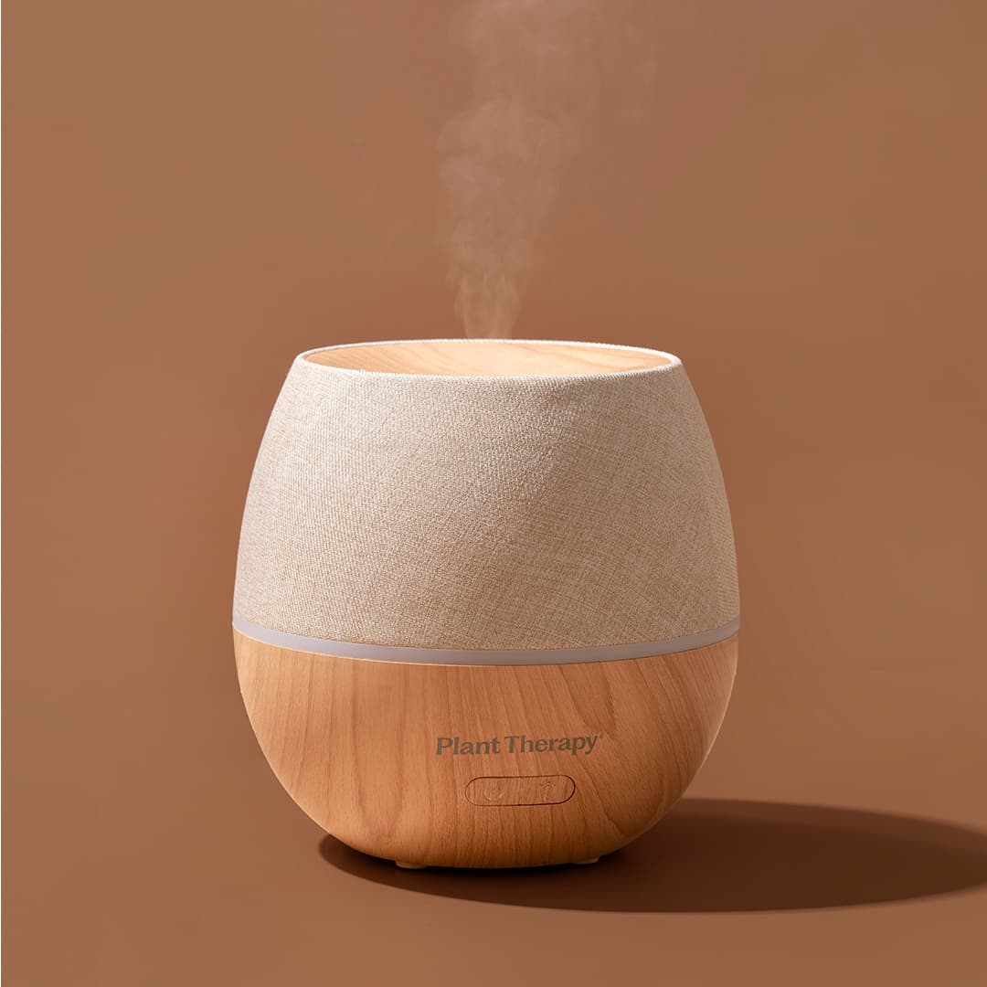 Close-up of diffuser releasing mist stream showing fabric top and wood bottom