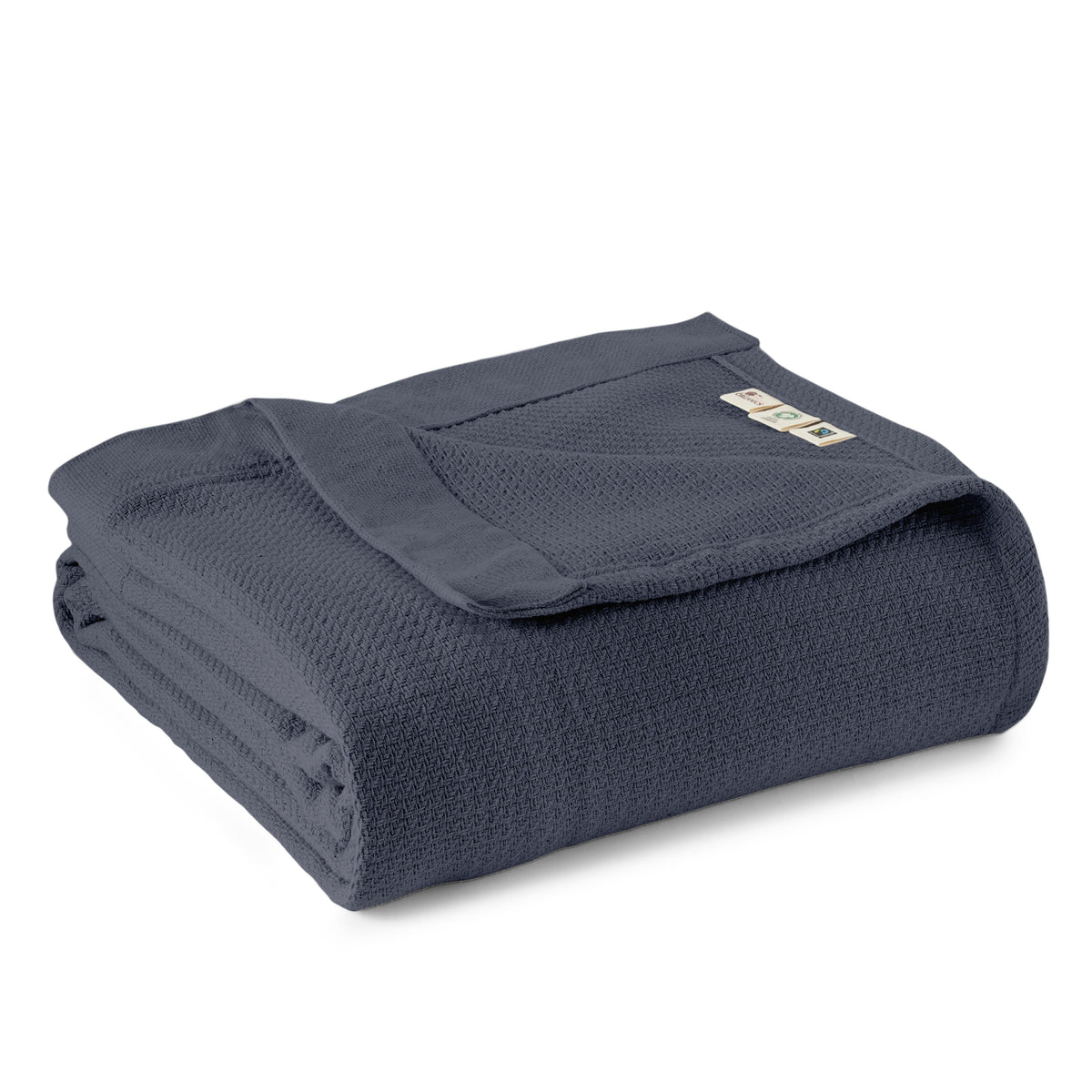 Slate blue-grey organic blanket folded to reveal detailed weave and three certification tags including GOTS