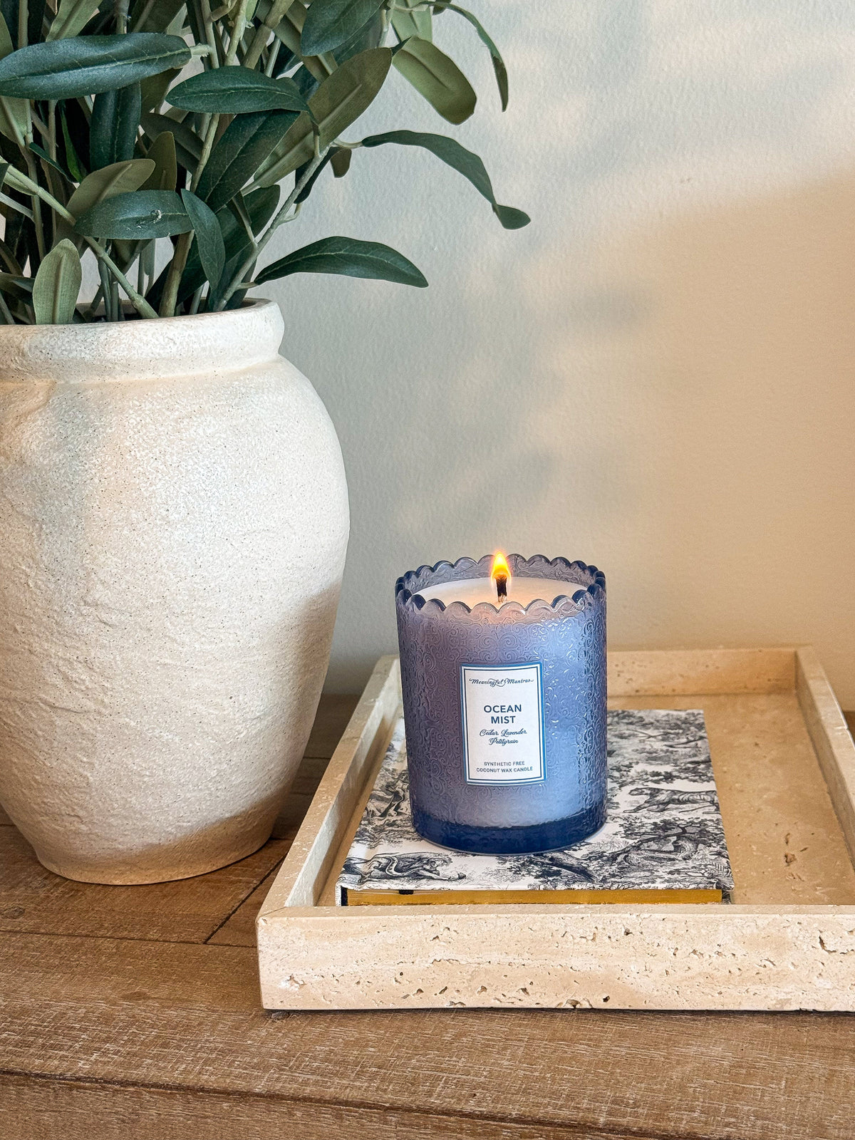 Blue glass candle burning on a book inside a travertine tray next to olive branches