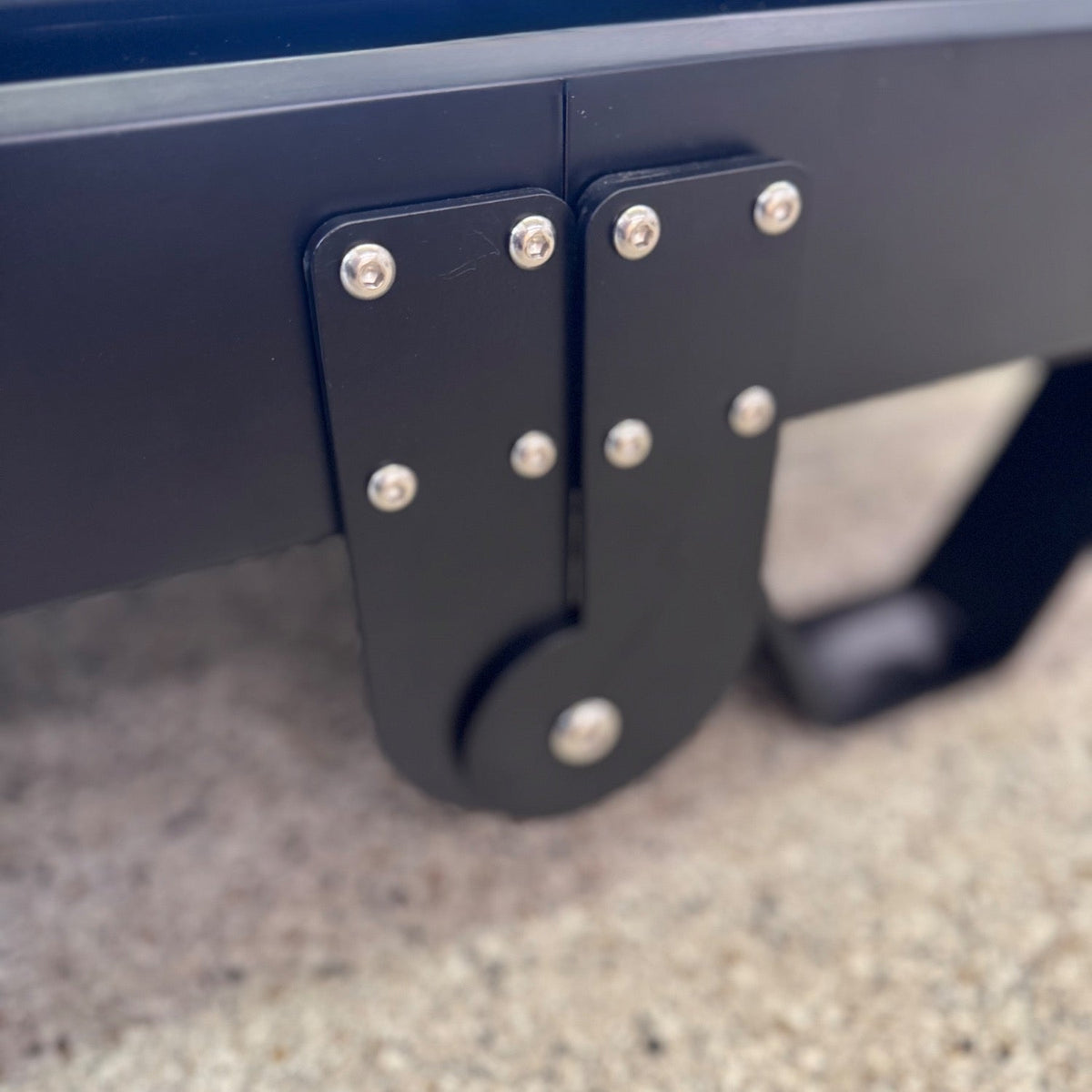 Detailed angle of heavy-duty black folding hinge mechanism attached to reformer base with multiple silver bolts for stability