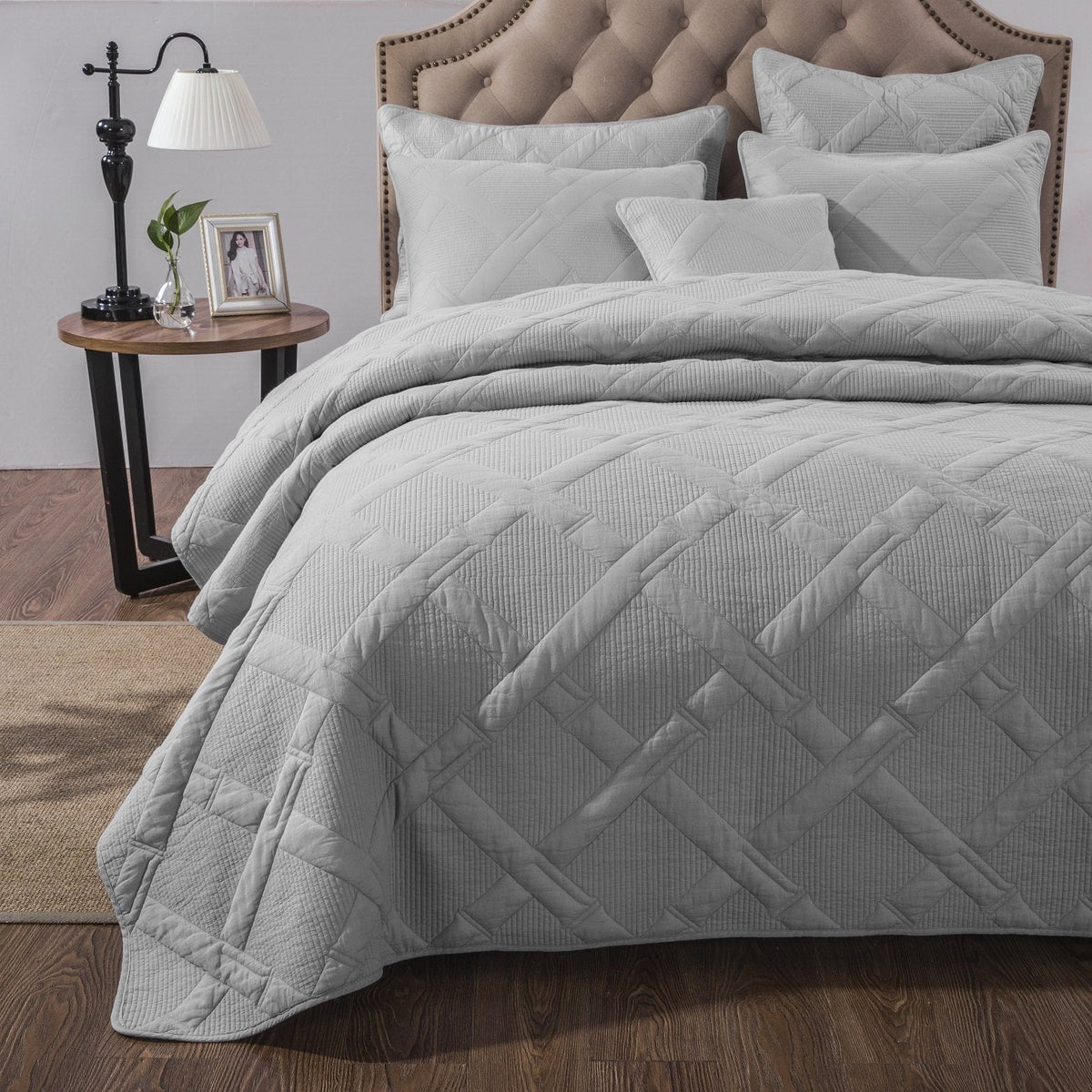 Three-quarter view of light gray cotton quilt set on a beige tufted headboard, highlighting layered pillows and raised