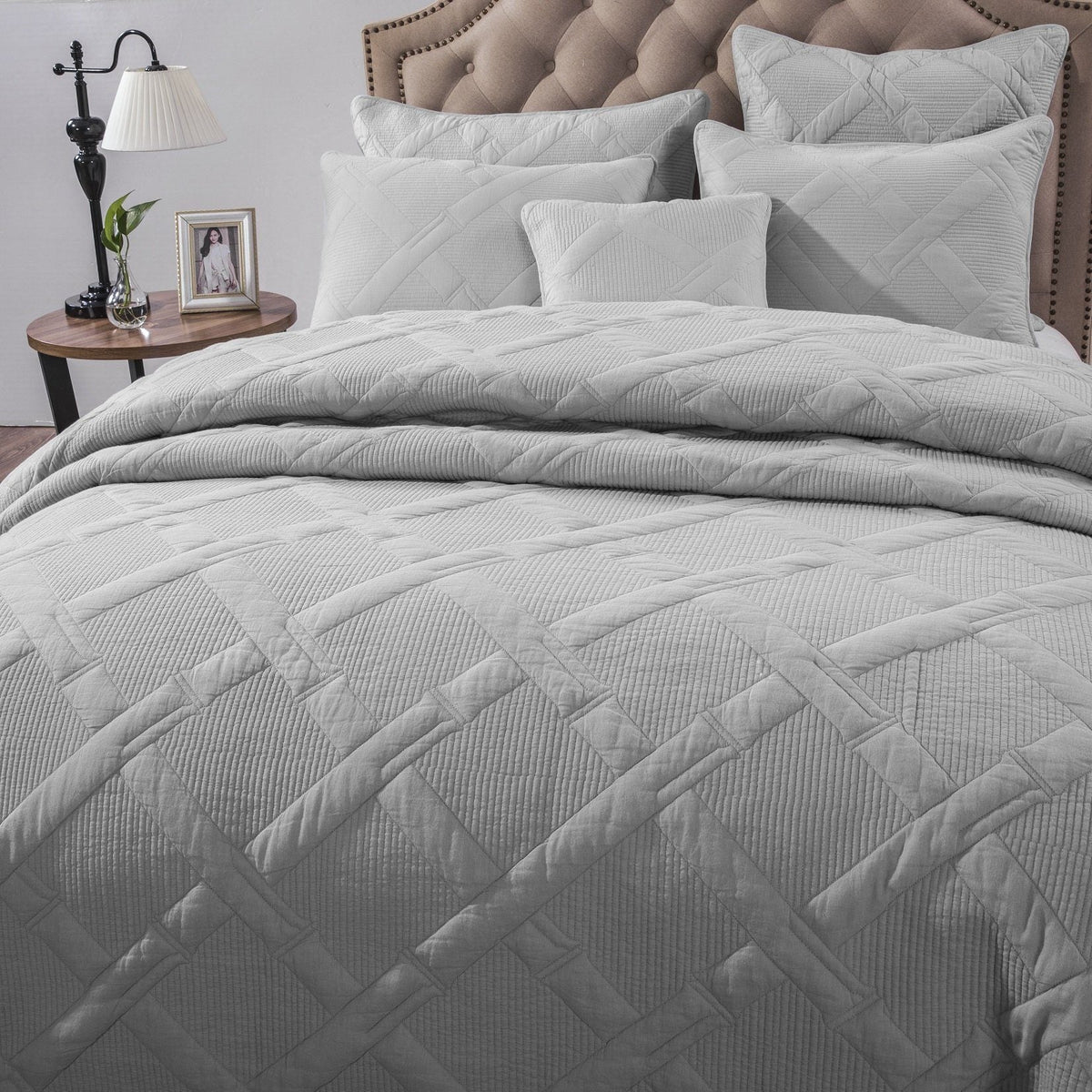 Close-up of light gray quilted comforter and stacked pillows against a tufted headboard, emphasizing soft fabric texture and