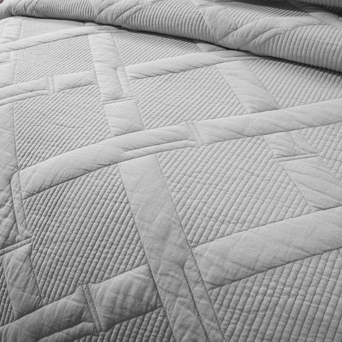 Extreme macro close-up of light gray cotton fabric showing precision quilting with raised diagonal lines forming a diamond