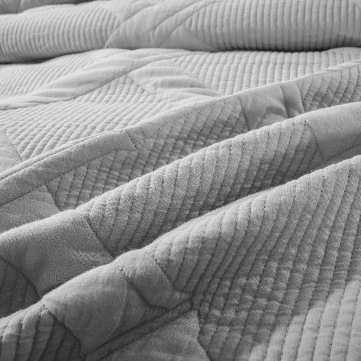 Macro detail of light gray quilted bedspread fabric, displaying raised ridges and visible stitching lines that emphasize the