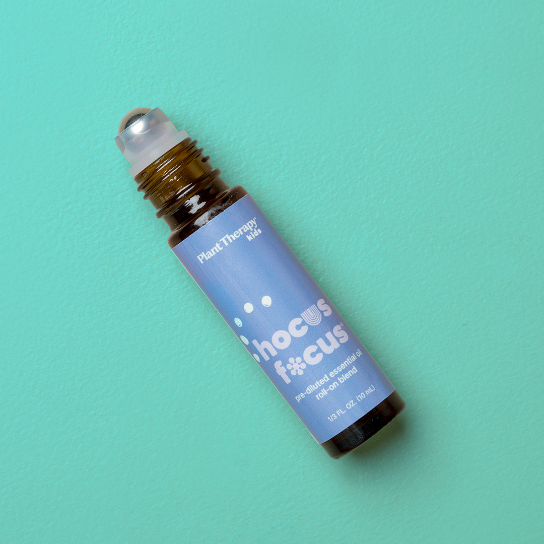 Amber Hocus Focus roll-on bottle on teal background showing clear cap and periwinkle label with playful white typography