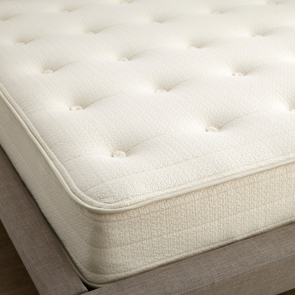Close-up of cream organic cotton mattress corner showing geometric quilted pattern, deep tufting buttons, and piped edge trim