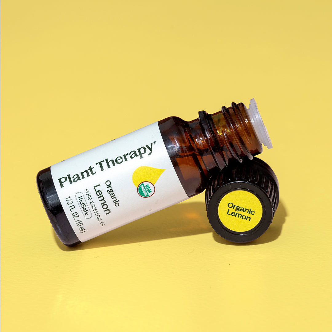 Single 10mL organic lemon essential oil bottle on yellow surface with black cap removed showing sticker