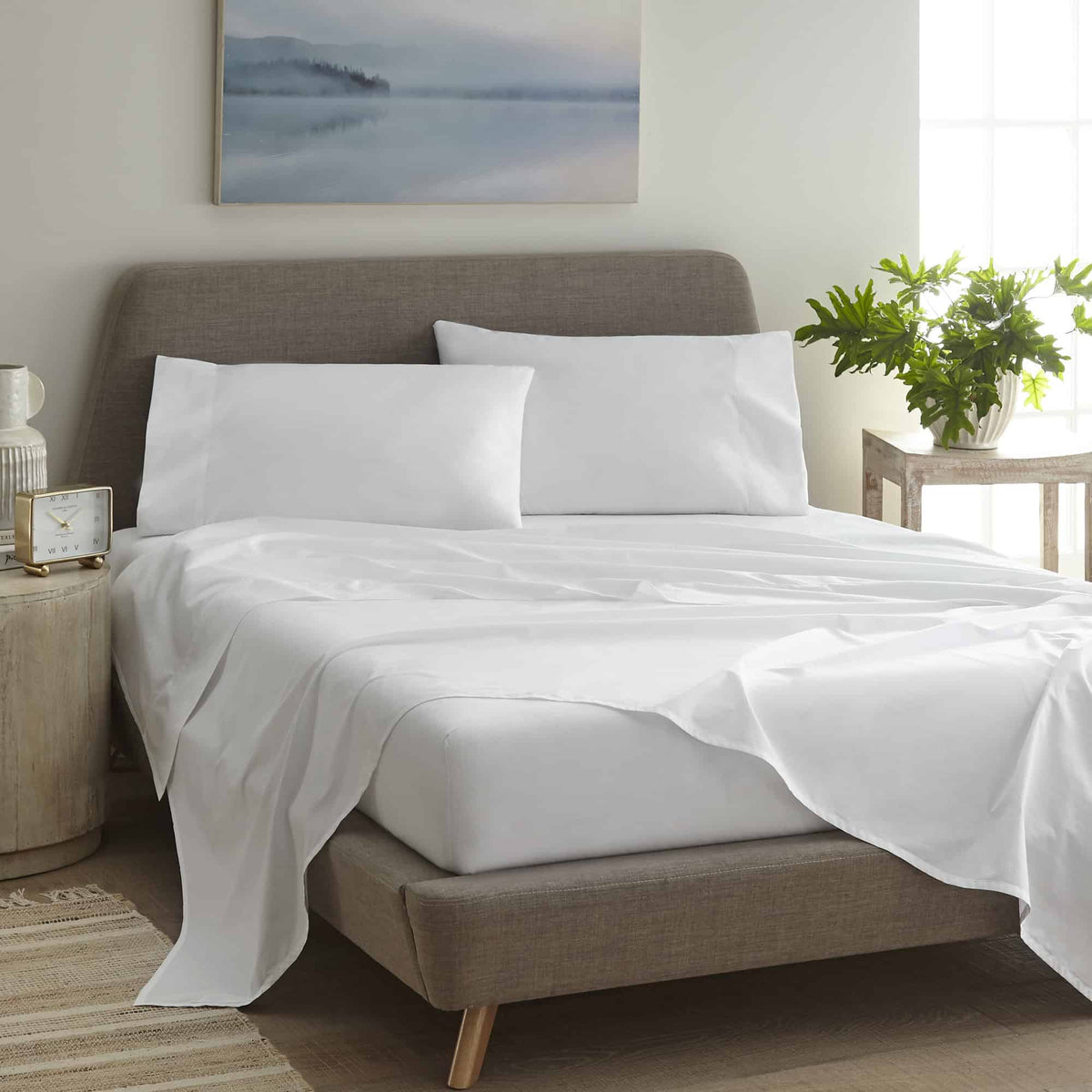 Made bed with white percale sheets, flat sheet draped, in bright bedroom with art